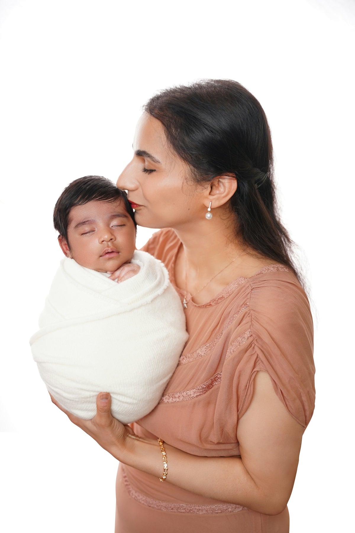 Mother kissing her newborn baby wrapped in a blanket.